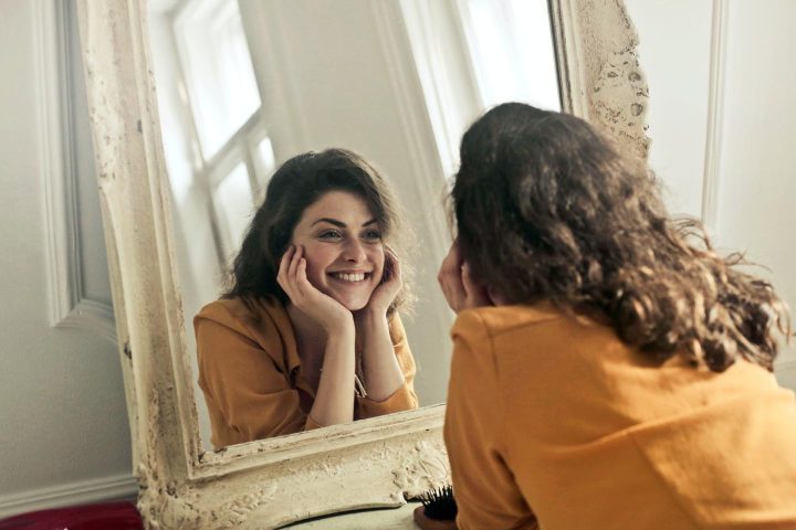 A woman looking into a mirror with a positive smile
