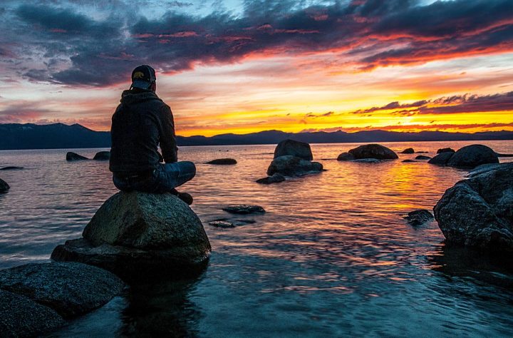 A man at sunset sitting on a stone at a beach, expressing serenity